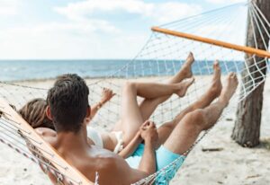 couple of tourists relaxing in hammock on beach near the sea