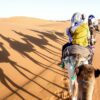 Tourists caravan riding dromedaries through sand dunes in Sahara desert