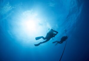 Two Silhouetted Diver Ascend an Anchor Line at the End of a Scuba Dive