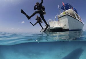 Over/under view showing divers performing giant stride entry into the clear calm waters of the