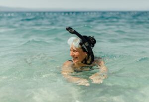 Cheerful woman wearing diving mask and snorkel swimming in water.