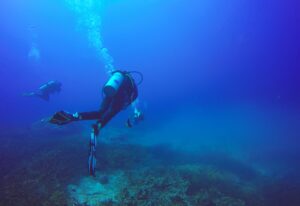 Scuba Divers swimming over the live coral reef full of fish and sea anemones.